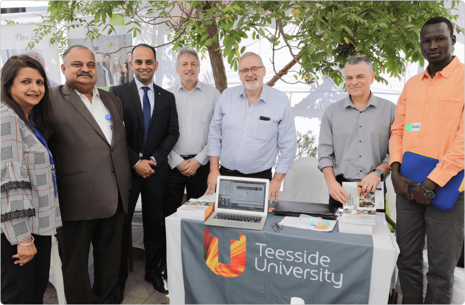 A group of people consisting of counsellors, university delegates, and financial advisors posing happily at an exhibition.